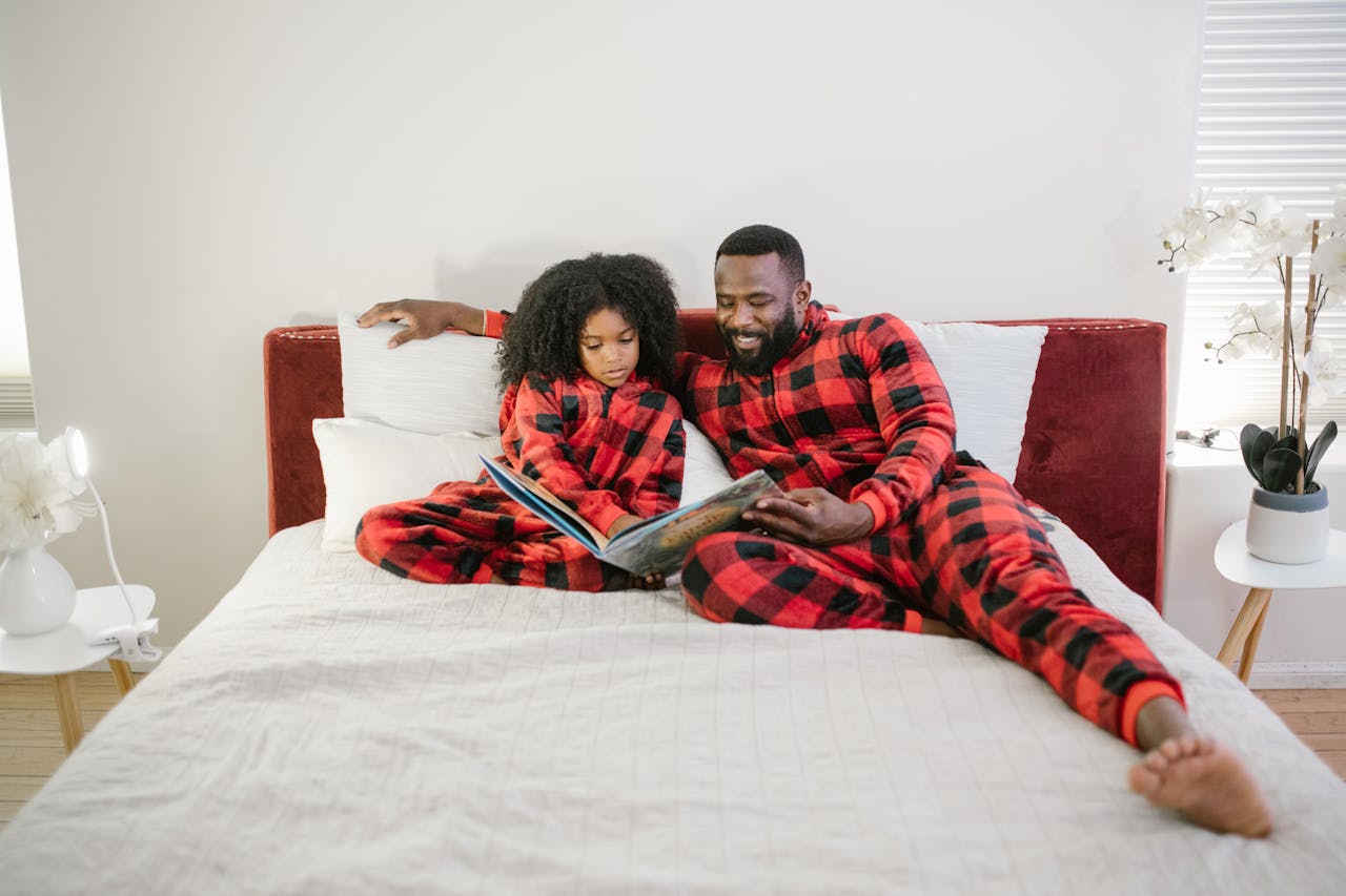 Father and daughter in matching pajamas enjoying a bedtime story together in a cozy bedroom setting.